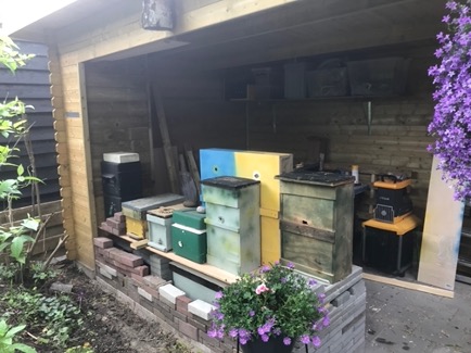 Overkapping met daaronder een aantal houten kasten die lijken op bijenkasten. Deze overkapping lijkt nogal op een schuur waarvan één kant open is.