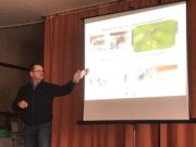 Scherm met dia van een presentatie met daarop enkele foto's van wespen en de tekst 'Wie siehen die Tiere aus?' Links van het scherm staat een man die duidelijk aan het vertellen is over deze dia, met zijn linkerhand die wijst op het scherm.